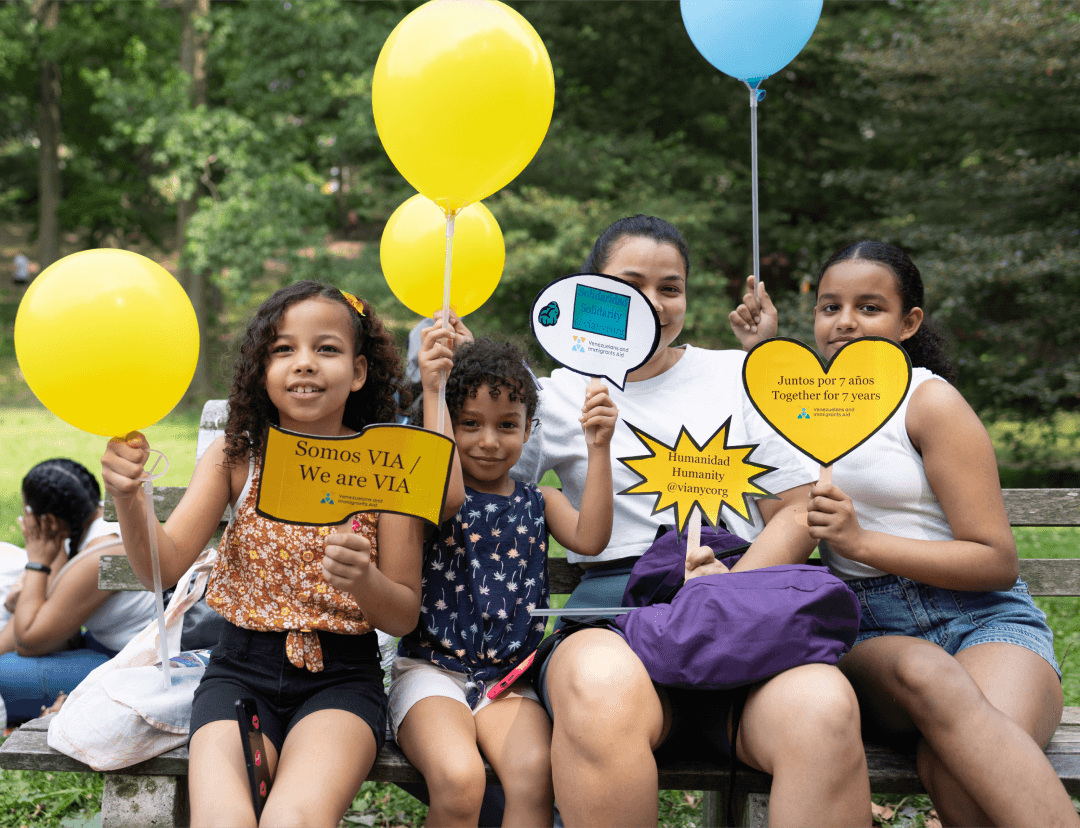 A joyful immigrant family celebrates VIA’s anniversary with balloons and handmade signs.