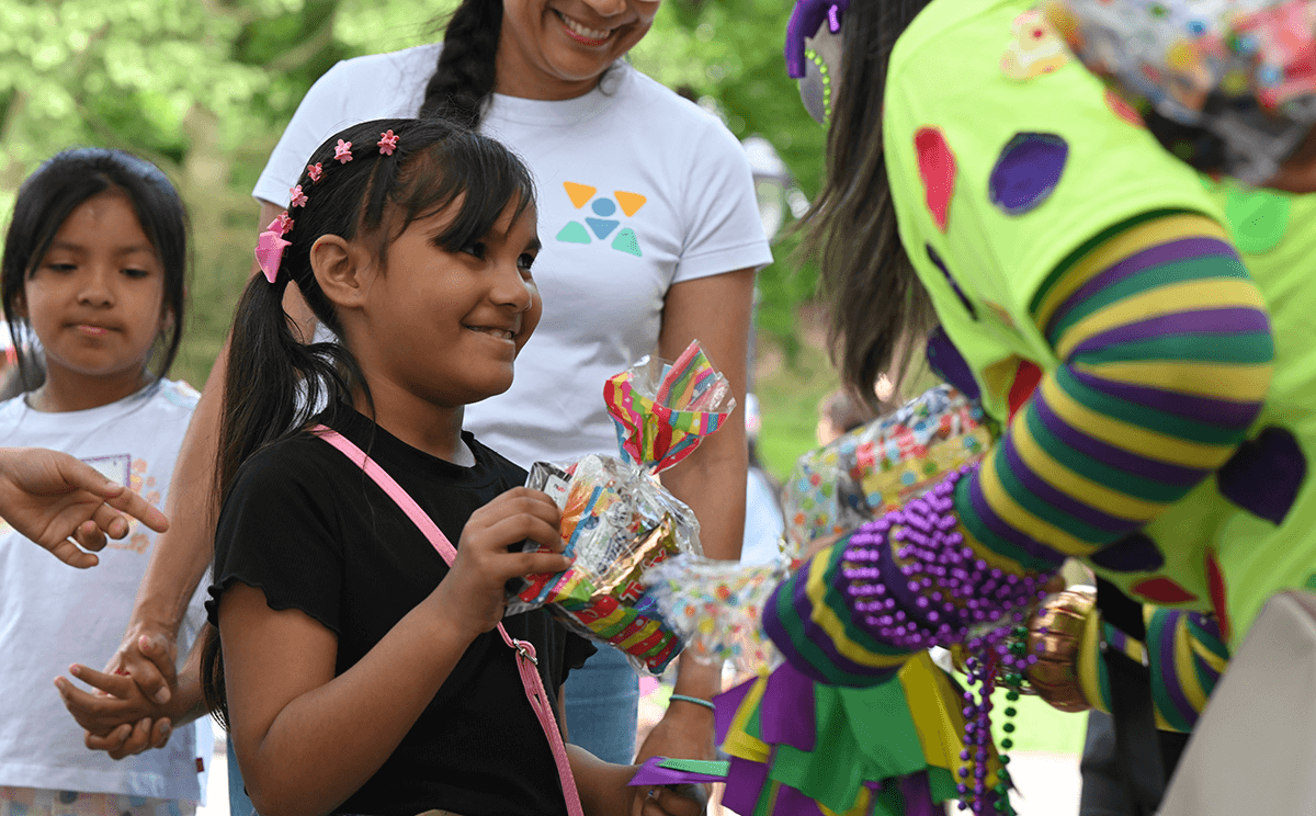 A VIA volunteer dressed as a party clown spreads joy by handing out ice cream to a young community member.
