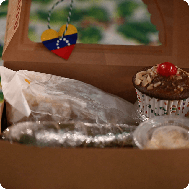 Close-up of a Venezuelan Christmas dinner box prepared by VIA, featuring traditional dishes and a heart-shaped tag with the Venezuelan flag.