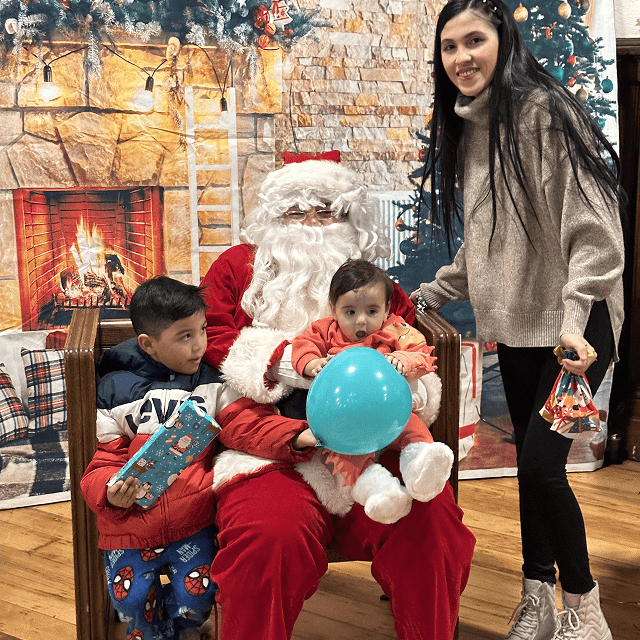 Santa Claus giving gifts to children during VIA’s Toy Drive with a parent joining the celebration.
