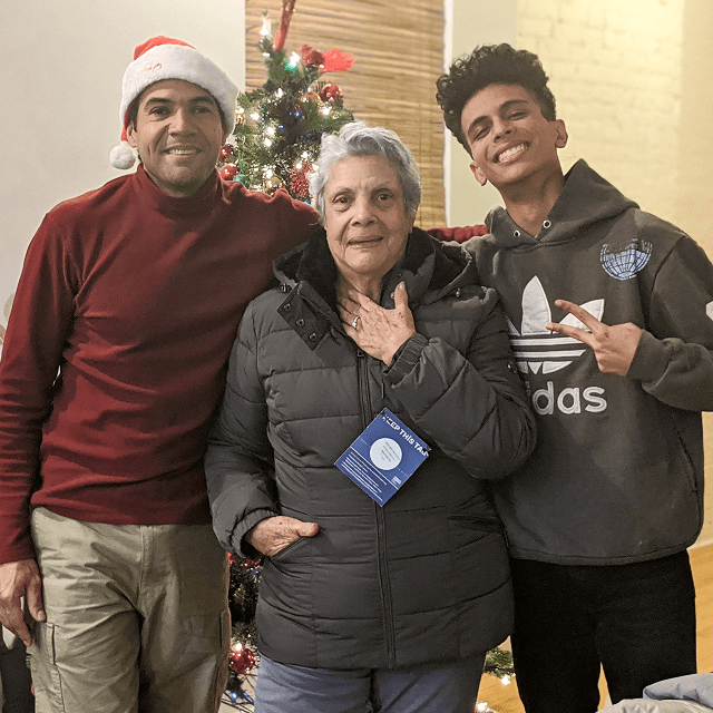 Three people smiling beside a Christmas tree after receiving a winter coat through VIA’s Annual Campaign.