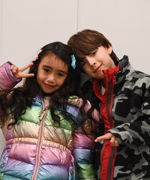 Two children smiling and posing in colorful winter jackets received through VIA’s Winter Coat Drive.