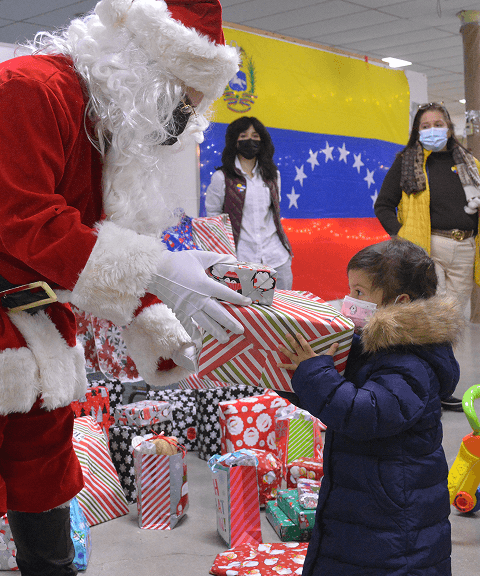 Santa Claus giving a wrapped gift to a young child during VIA’s Toy Drive and Christmas celebration.